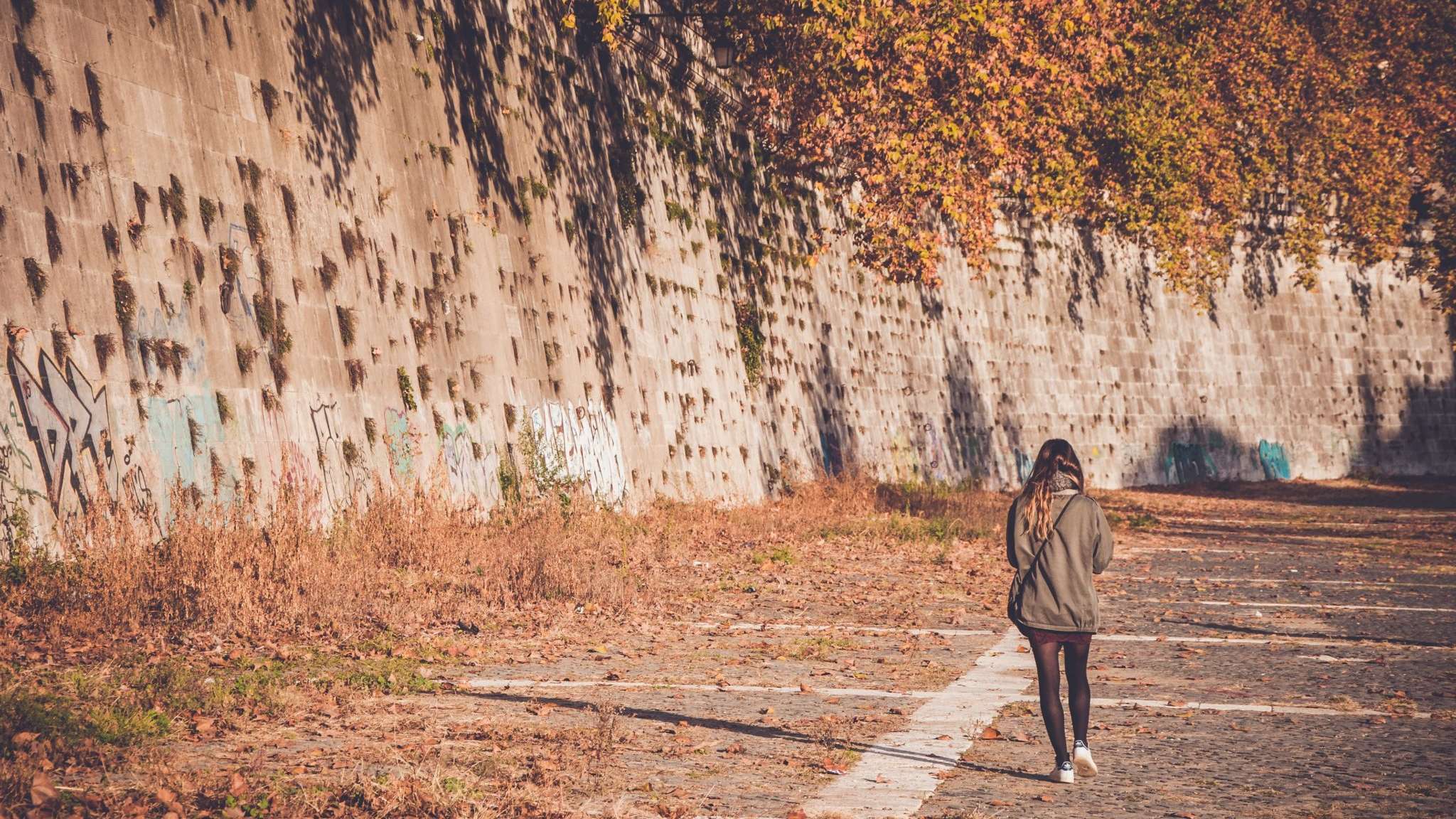 Woman walking down a road past concrete wall