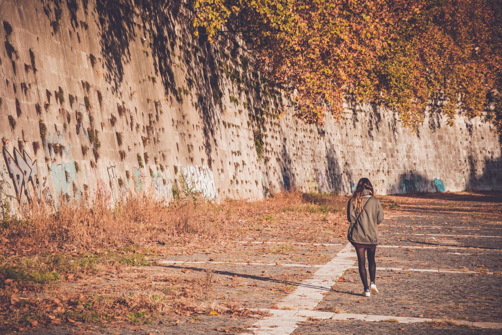 Woman walking down a road past concrete wall