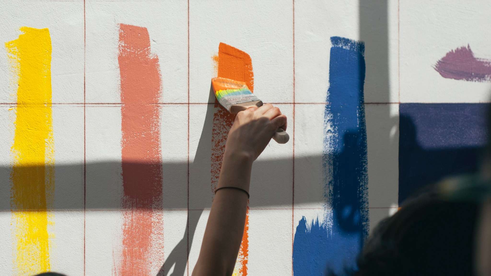 Painters using paint rollers to apply multiple lines of paint to a wall