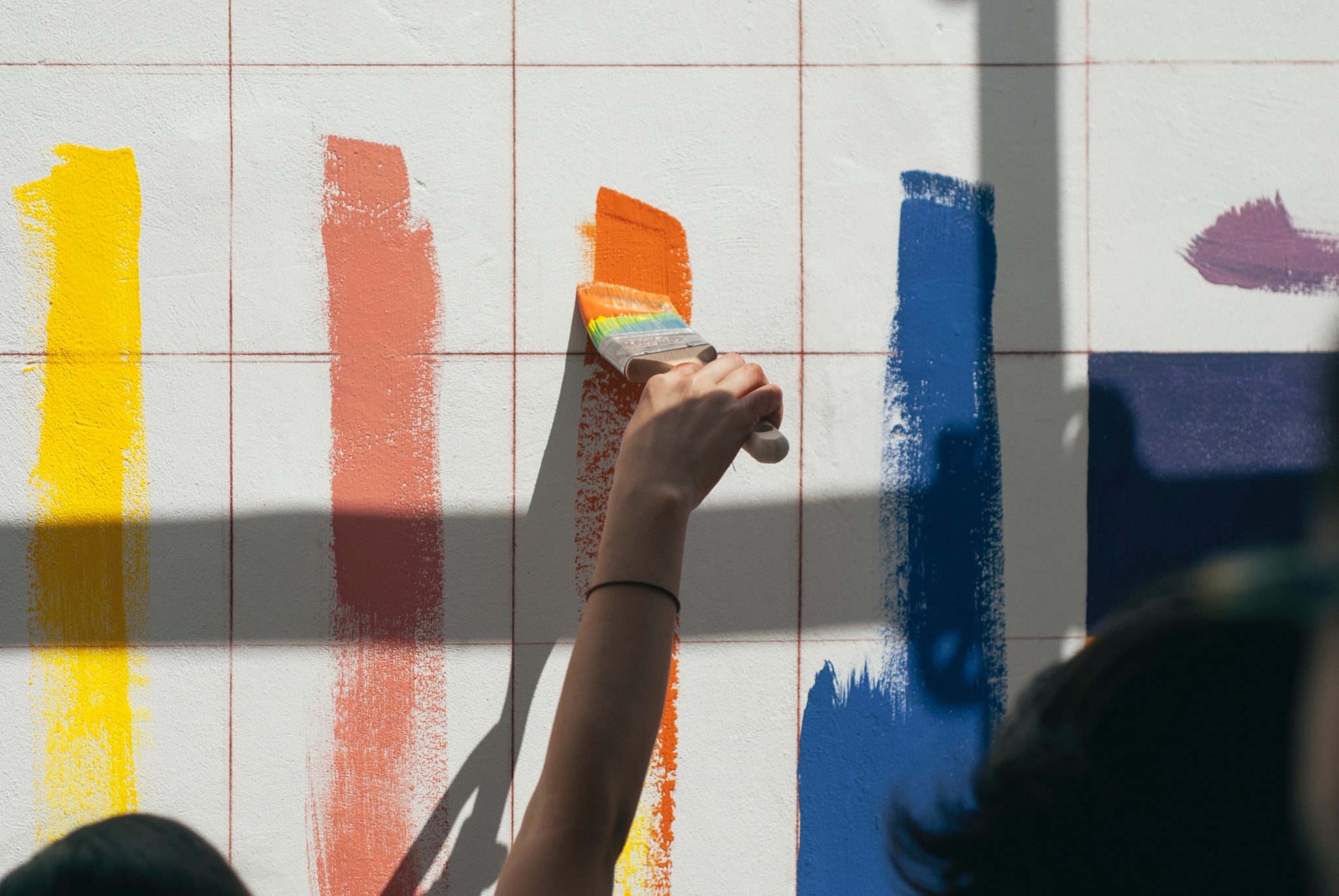 Painters using paint rollers to apply multiple lines of paint to a wall