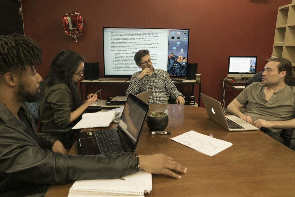 Students and instructor gathered around a table discussing a script