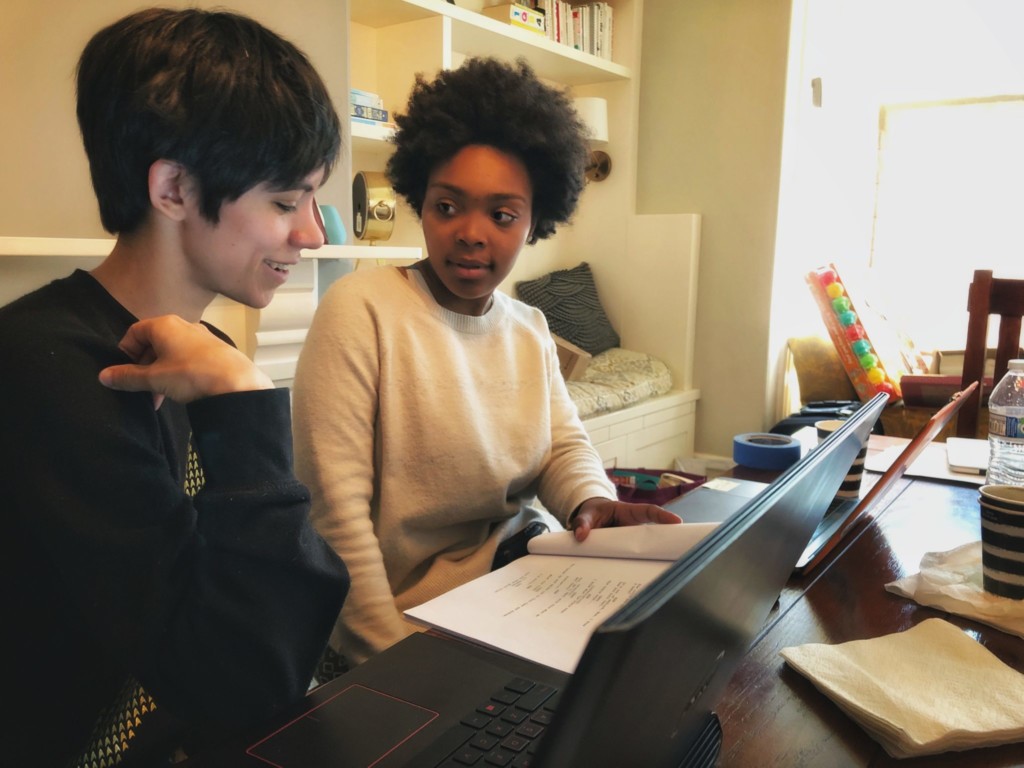 Two writing students discussing scripts on laptops