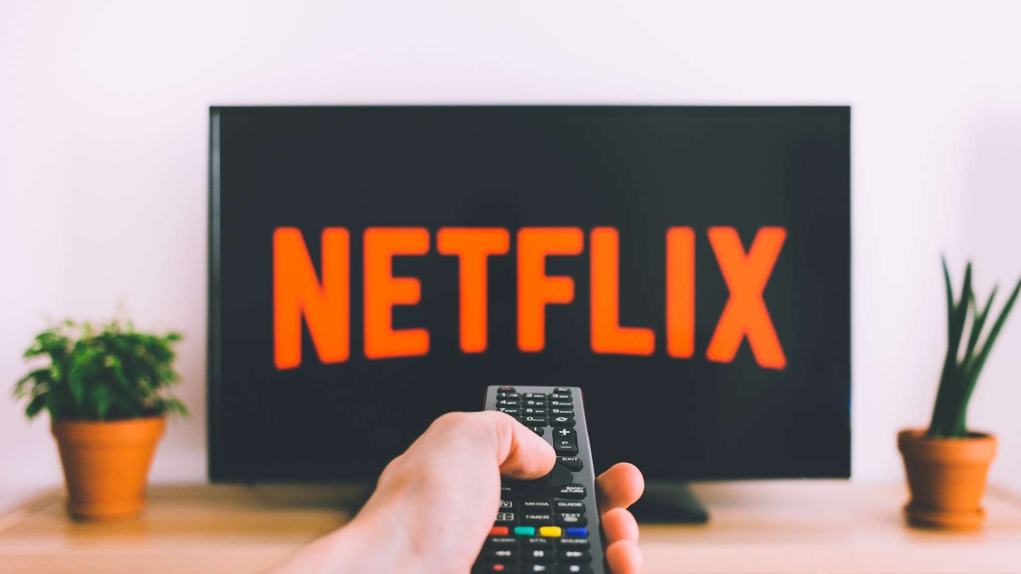 Hand pointing TV remote control at a screen showing Netflix on it