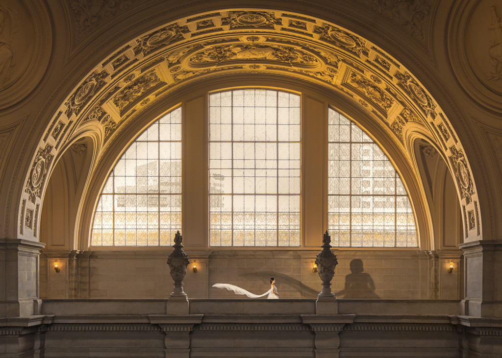 The huge arch in a building. Across the arch is a woman in white, her dress billows behind her.