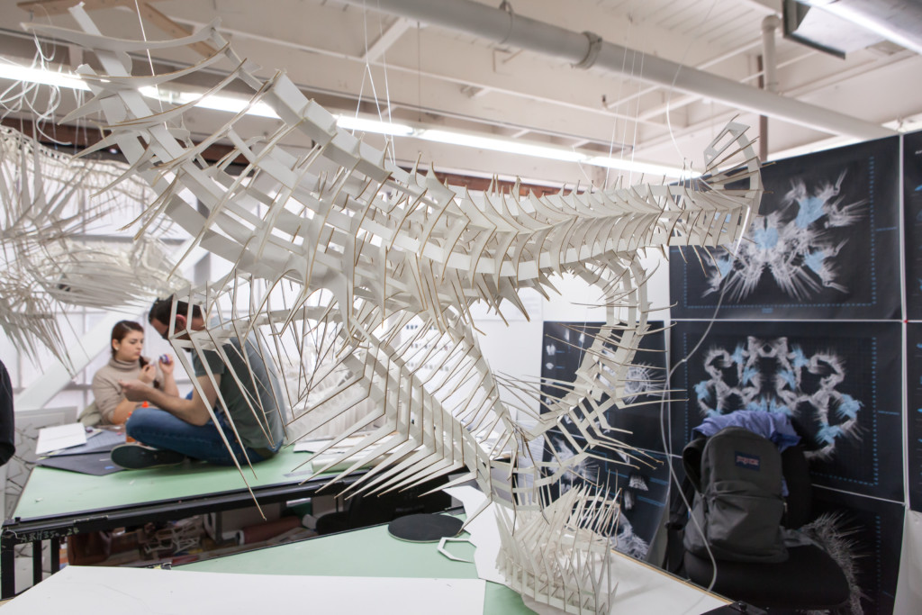 Students sitting on tables in a classroom behind a large sculpture