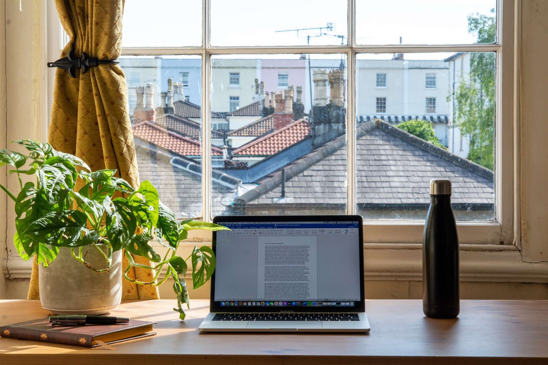 Work-at-home desk space with computer, potted plant and water bottle in front of a window in daytime